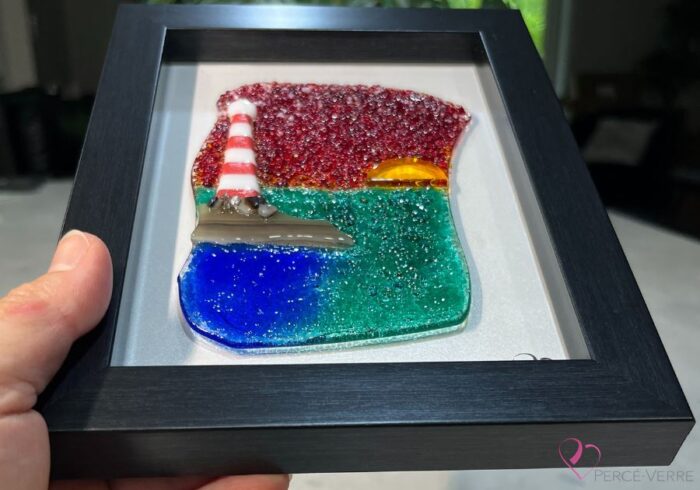 Work in fused glass representing a lighthouse under a blazing red sky, framed 5 x 7, Horizon de Percé-Verre collection.