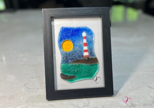 Work in fused glass depicting a lighthouse on a rock overlooking the turquoise sea, framed 5 x 7, Horizon de Percé-Verre collection.