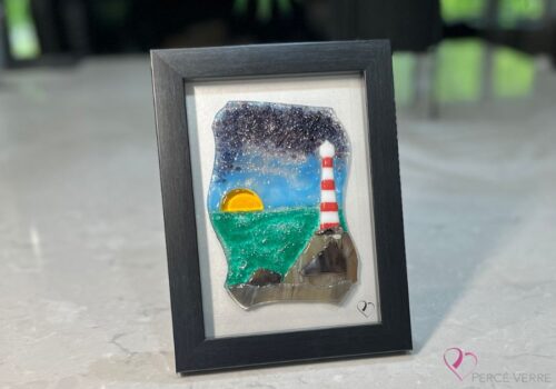 Phare No. 3 – Collection Horizon. Verre fusionné avec ciel mauve et coucher de soleil. Phare sur des rochers au bord de l’eau. Cadre 5 x 7, œuvre unique.