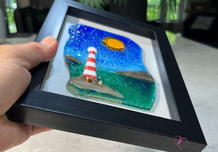 Work in fused glass representing a lighthouse by the sea, under a blue sky. Water and sky in harmony. 5 x 7 frame, Horizon collection.