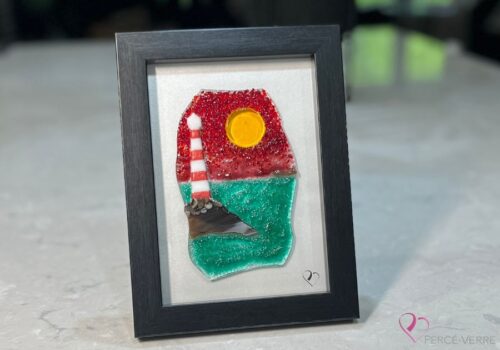 Work in fused glass depicting a lighthouse on a rock by the ocean, under a brilliant red sky. Horizon Collection, 5 x 7 frame.